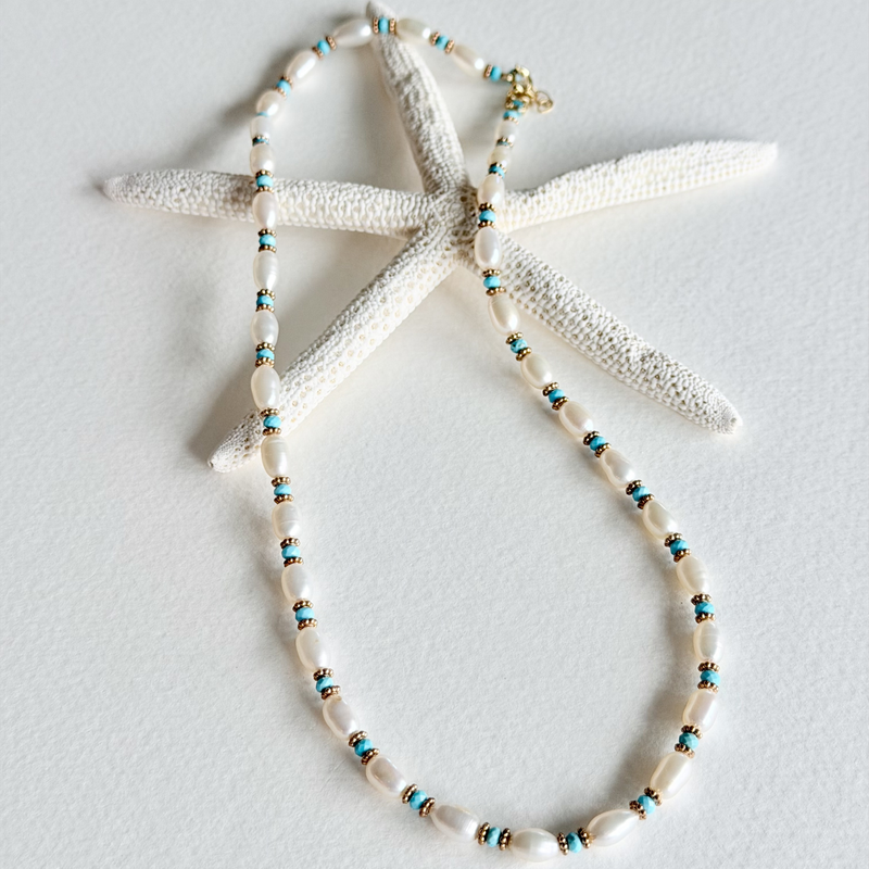 A beaded necklace with white shell-like beads and small turquoise and gold spacer beads, displayed on a white starfish prop against a light gray background.