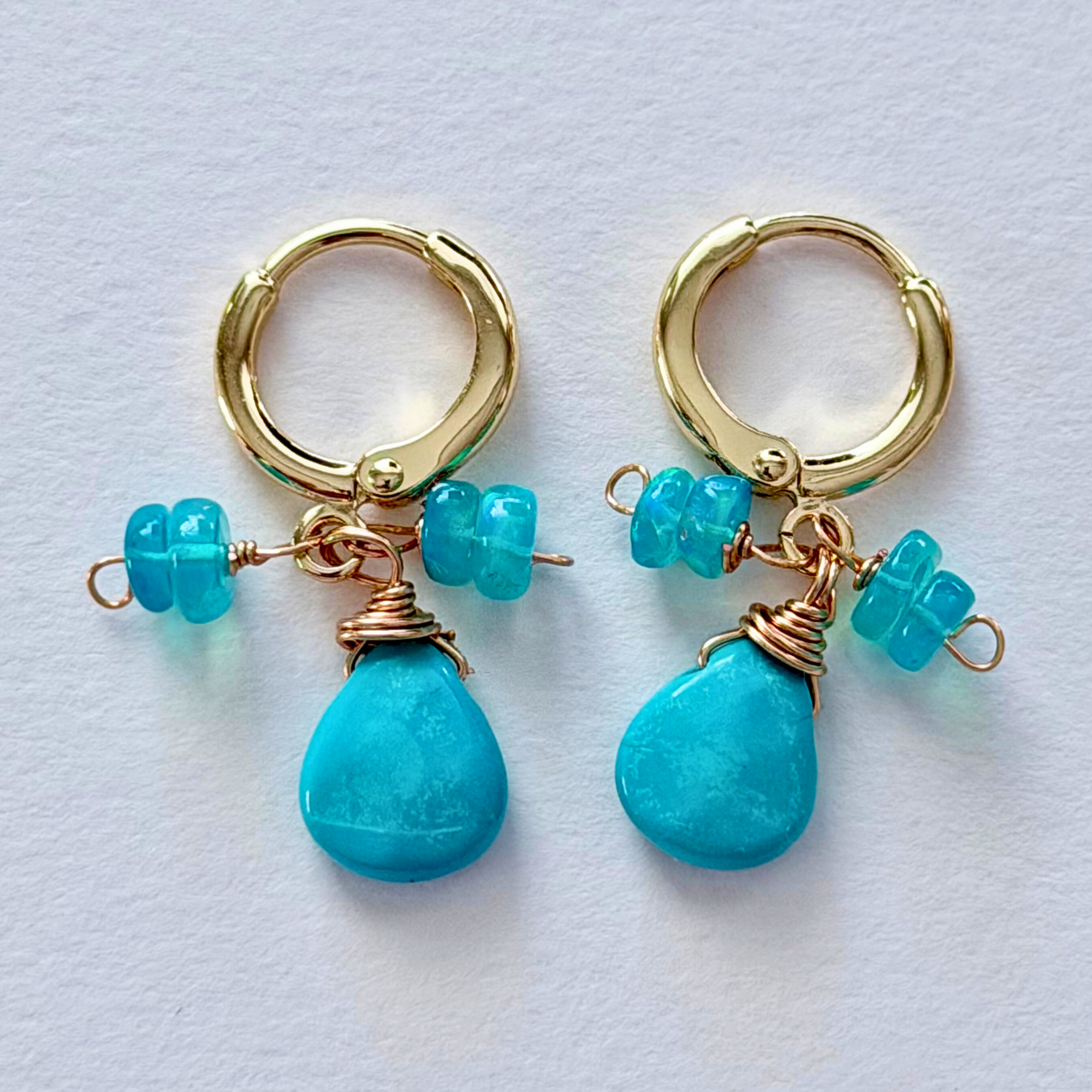 Gold hoop earrings with turquoise beads on a light blue background