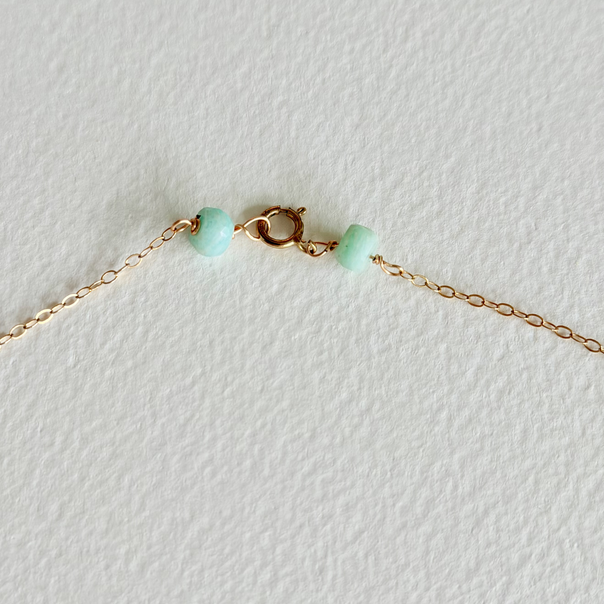 Gold chain close up with green beads on a light gray background