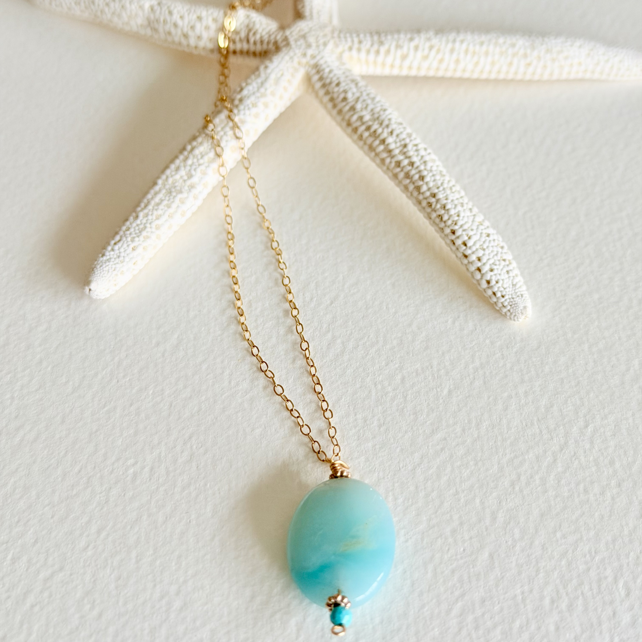 Turquoise pendant necklace on a gold chain with a starfish background