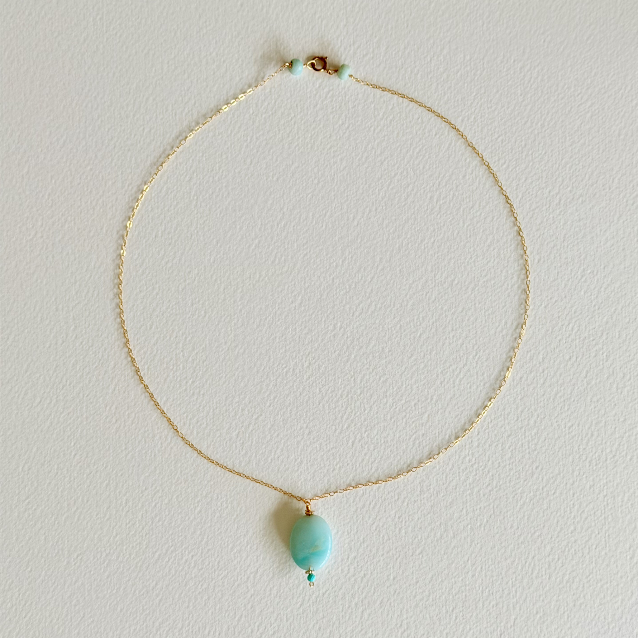 Gold necklace with a turquoise pendant on a light gray background