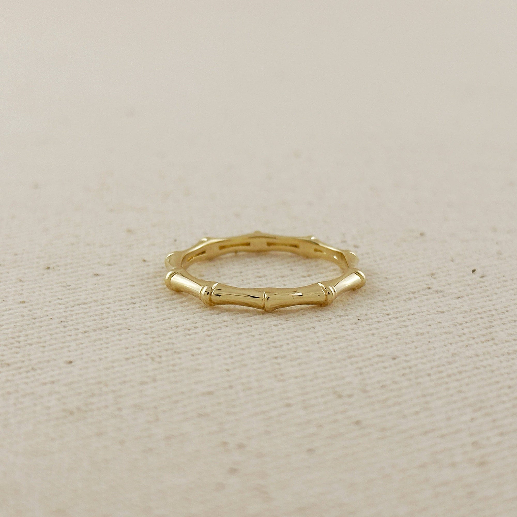 Gold ring with bamboo design on a beige fabric background