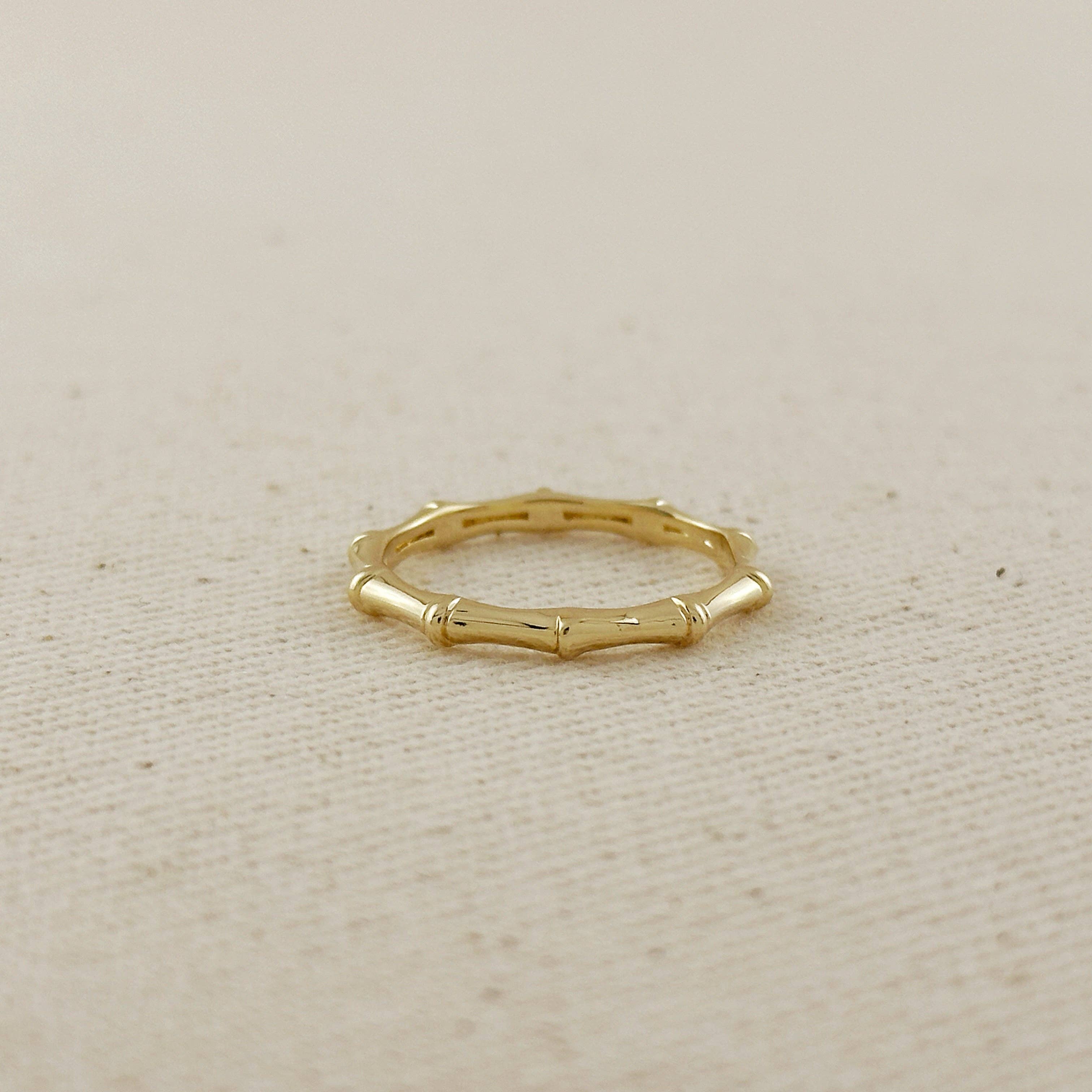 Gold ring with bamboo design on a beige fabric background