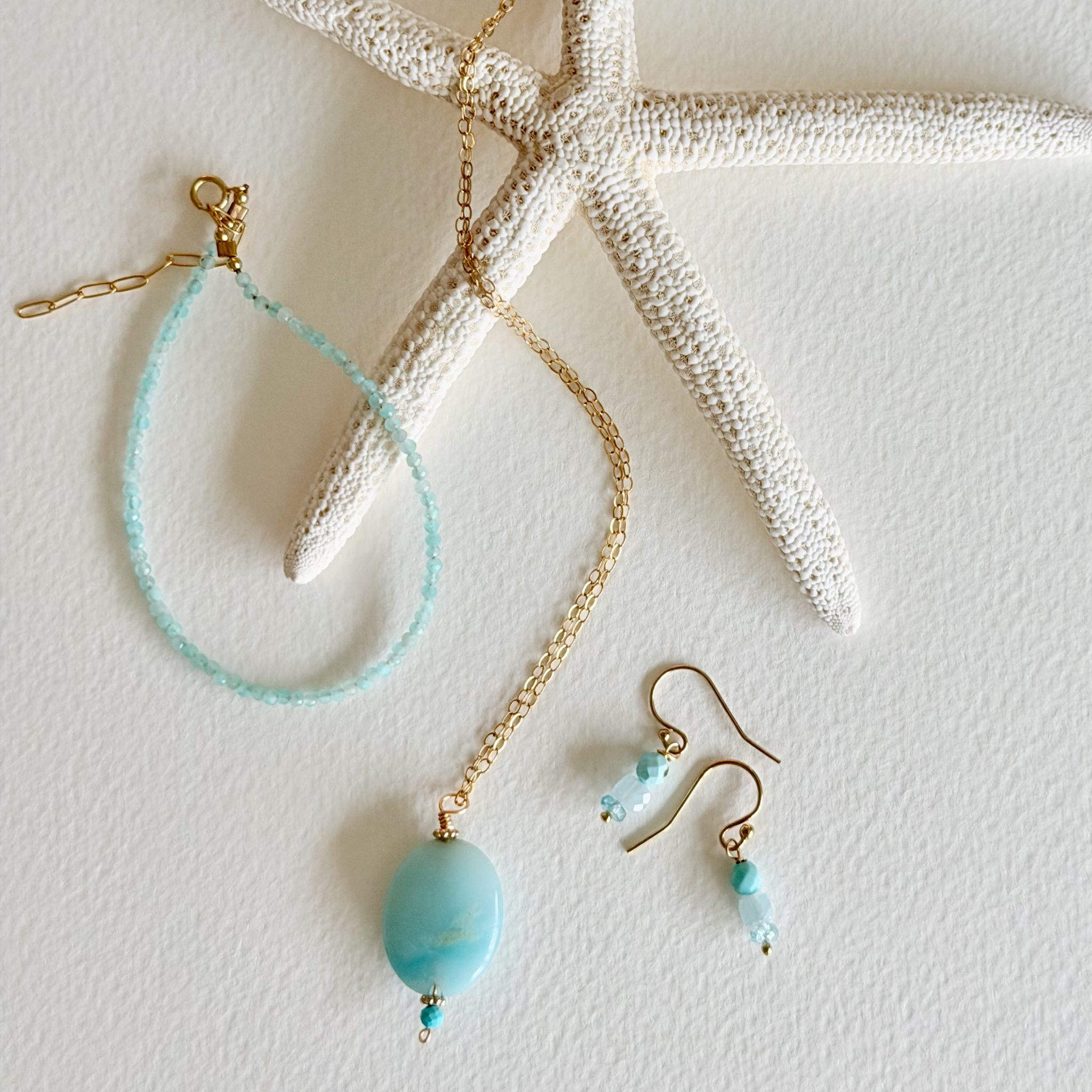 Jewelry set with turquoise beads and gold chains on a textured white surface.