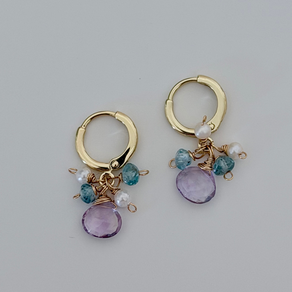 Gold hoop earrings with amethyst and blue beads on a light gray background