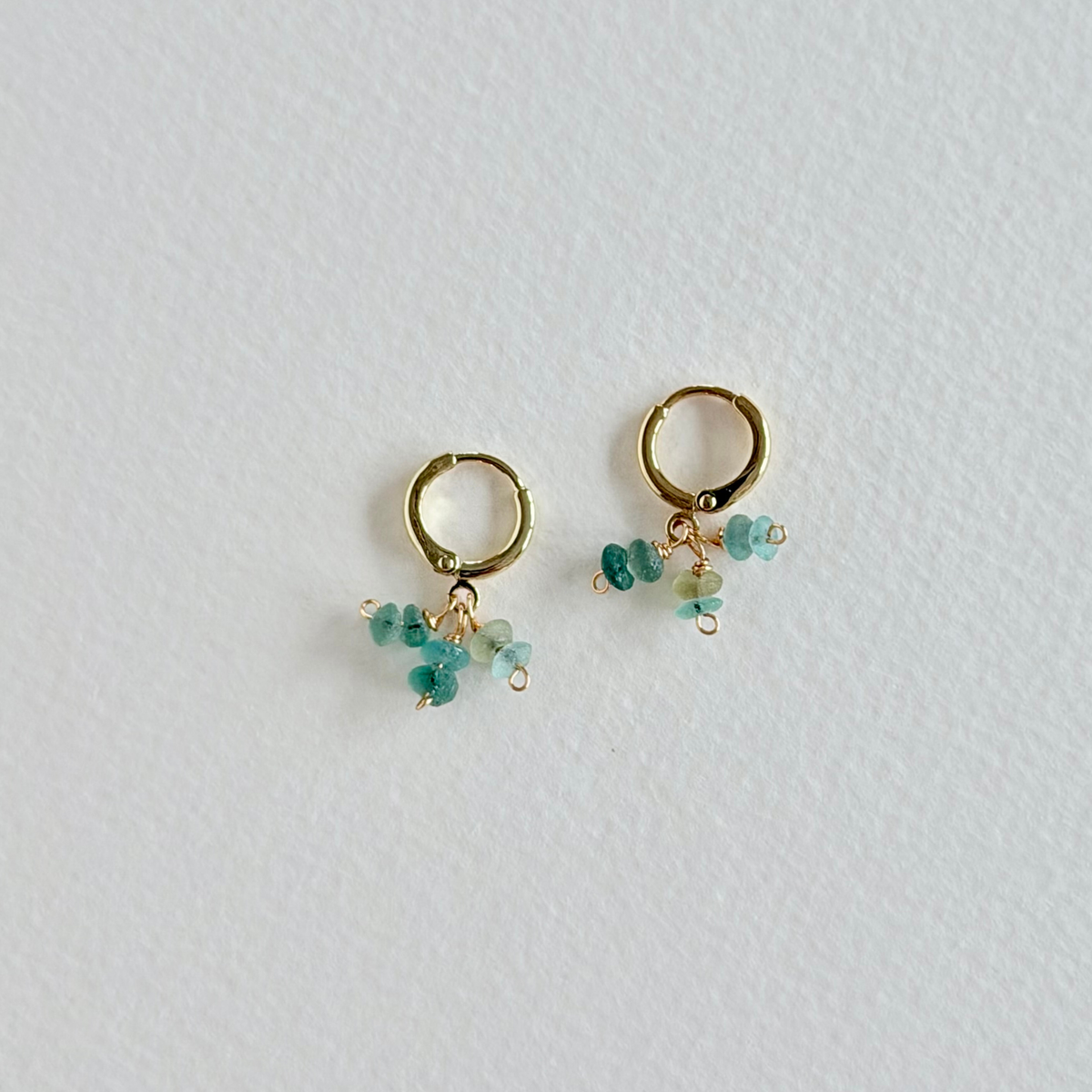 Gold earrings with green gemstones on a light gray background