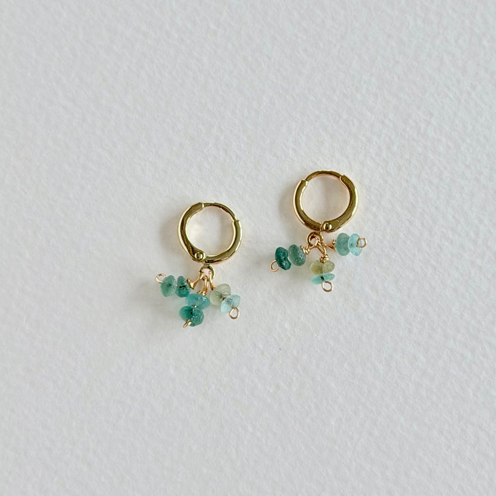 Gold hoop earrings with turquoise beads on a light gray background