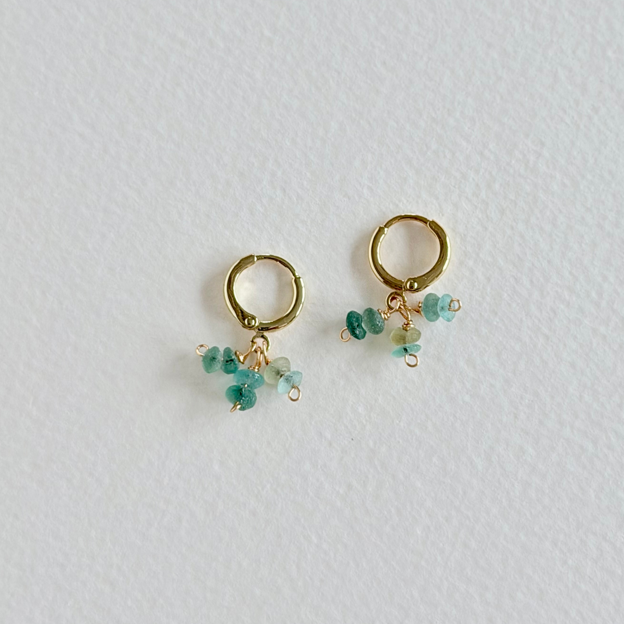 Gold hoop earrings with turquoise beads on a light gray background