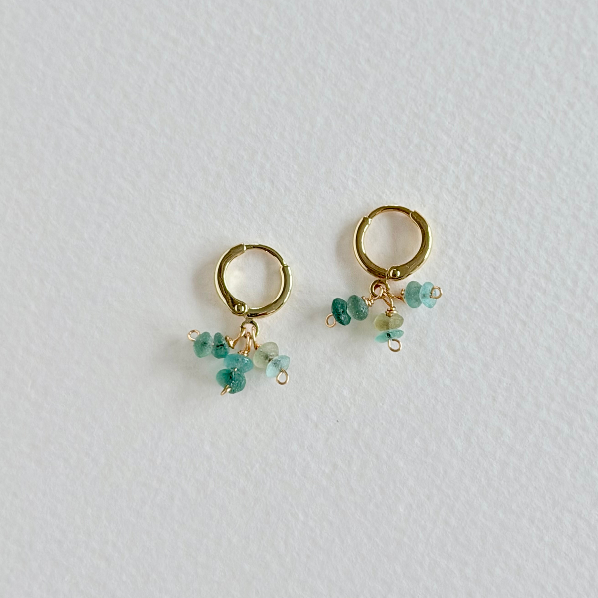 Gold hoop earrings with turquoise beads on a light gray background