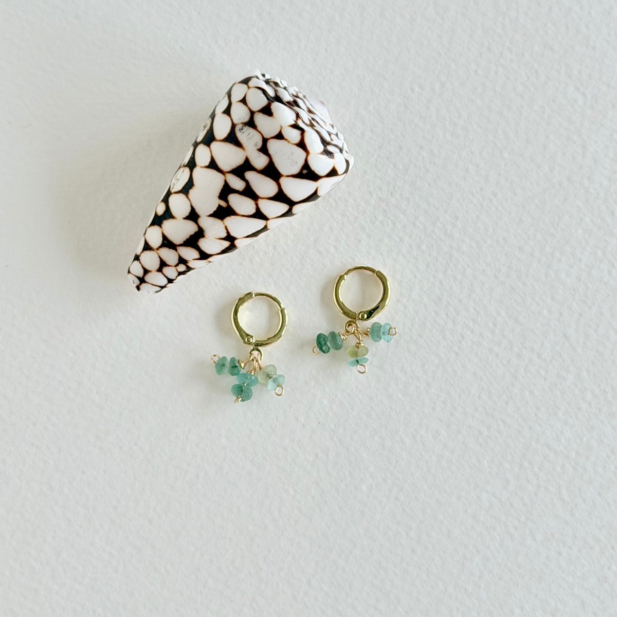 Pair of gold earrings with green beads on a light gray background