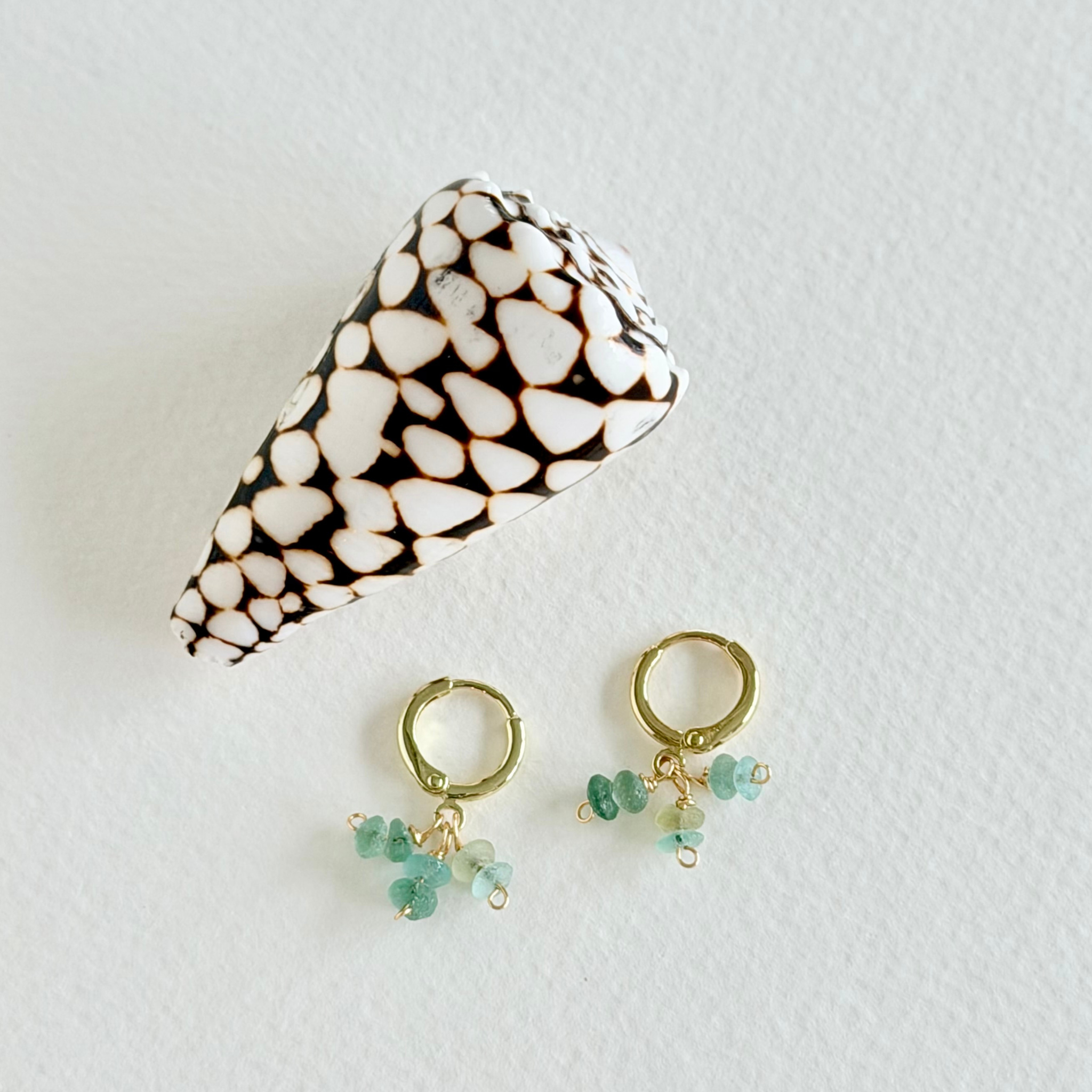 Gold earrings with green beads and a patterned case on a light background