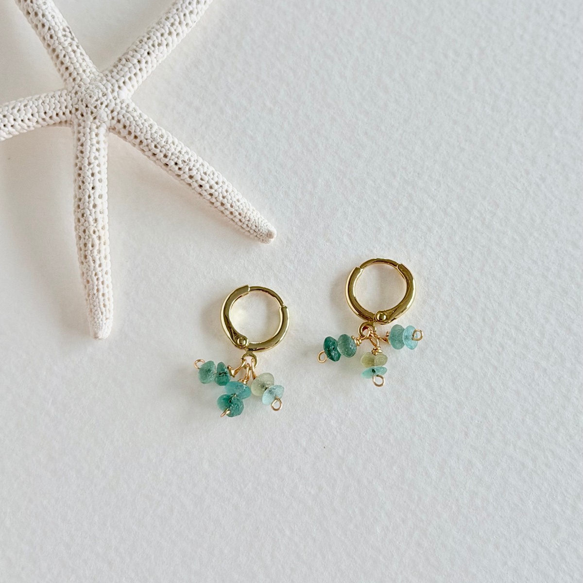 Gold hoop earrings with green beads on a white background with a starfish.