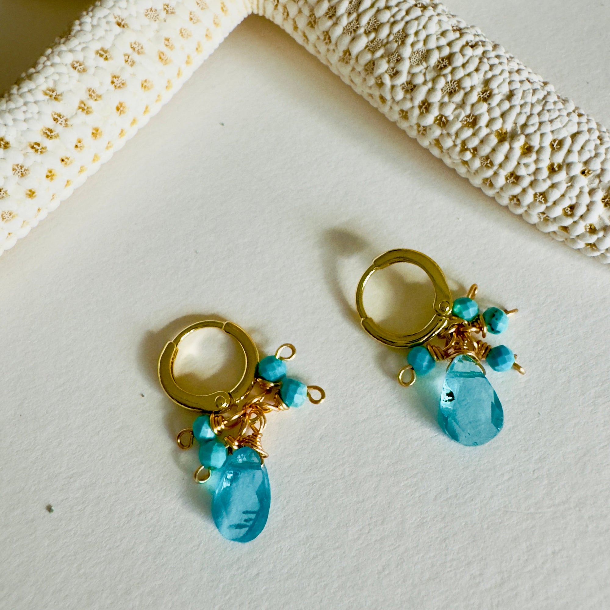 Gold earrings with blue teardrop beads on a textured surface