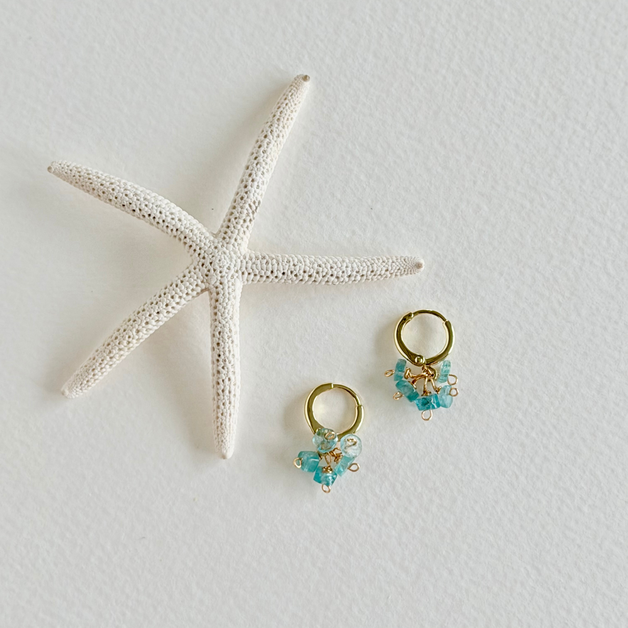 Gold hoop earrings with aquamarine gemstones on a white surface with a starfish.