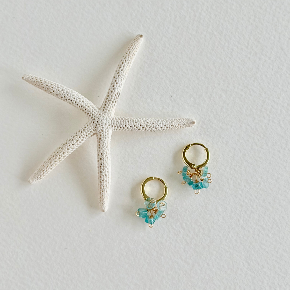 Gold hoop earrings with aquamarine gemstones on a white surface with a starfish.
