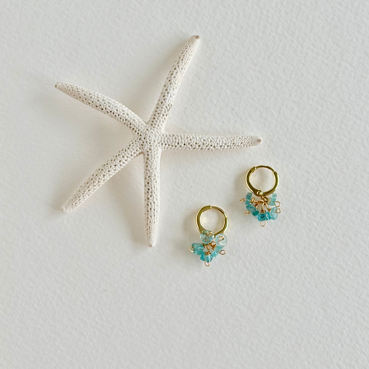 Gold hoop earrings with aquamarine stones on a white background with a starfish.