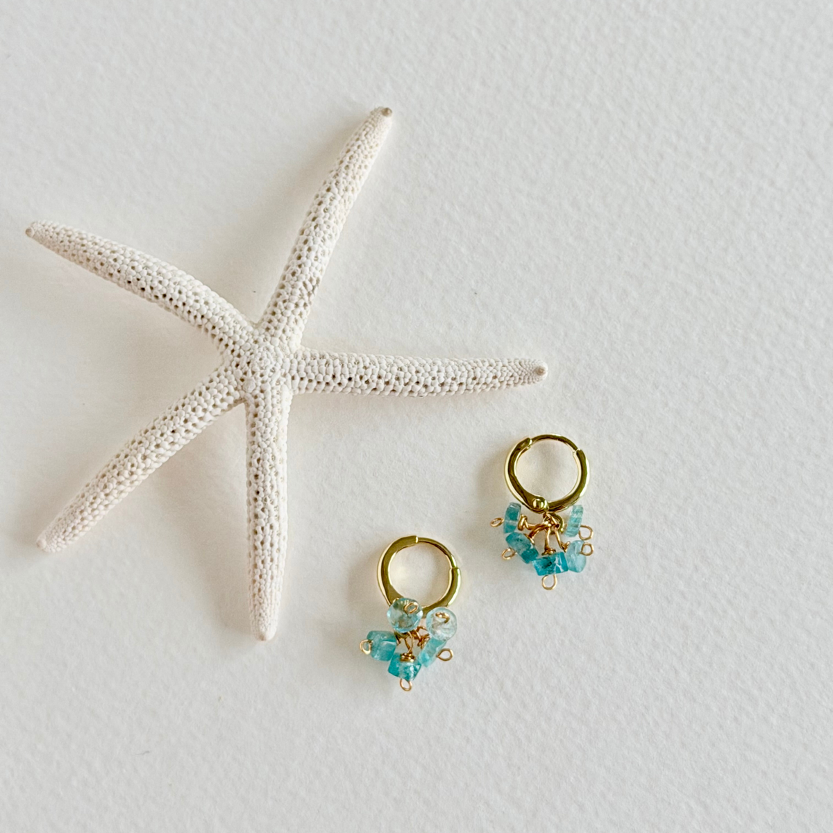 Gold and aquamarine earrings with a starfish on a light background