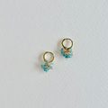 Gold hoop earrings with aquamarine gemstones on a light gray background