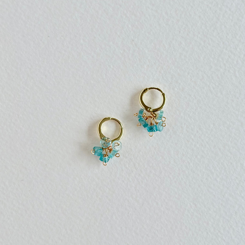 Gold hoop earrings with aquamarine gemstones on a light gray background
