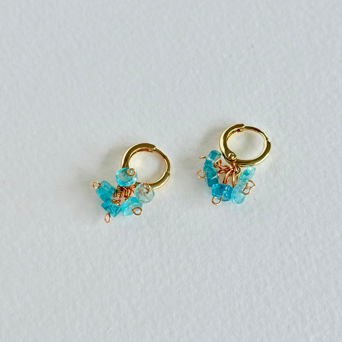 Gold hoop earrings with aquamarine beads on a light gray background