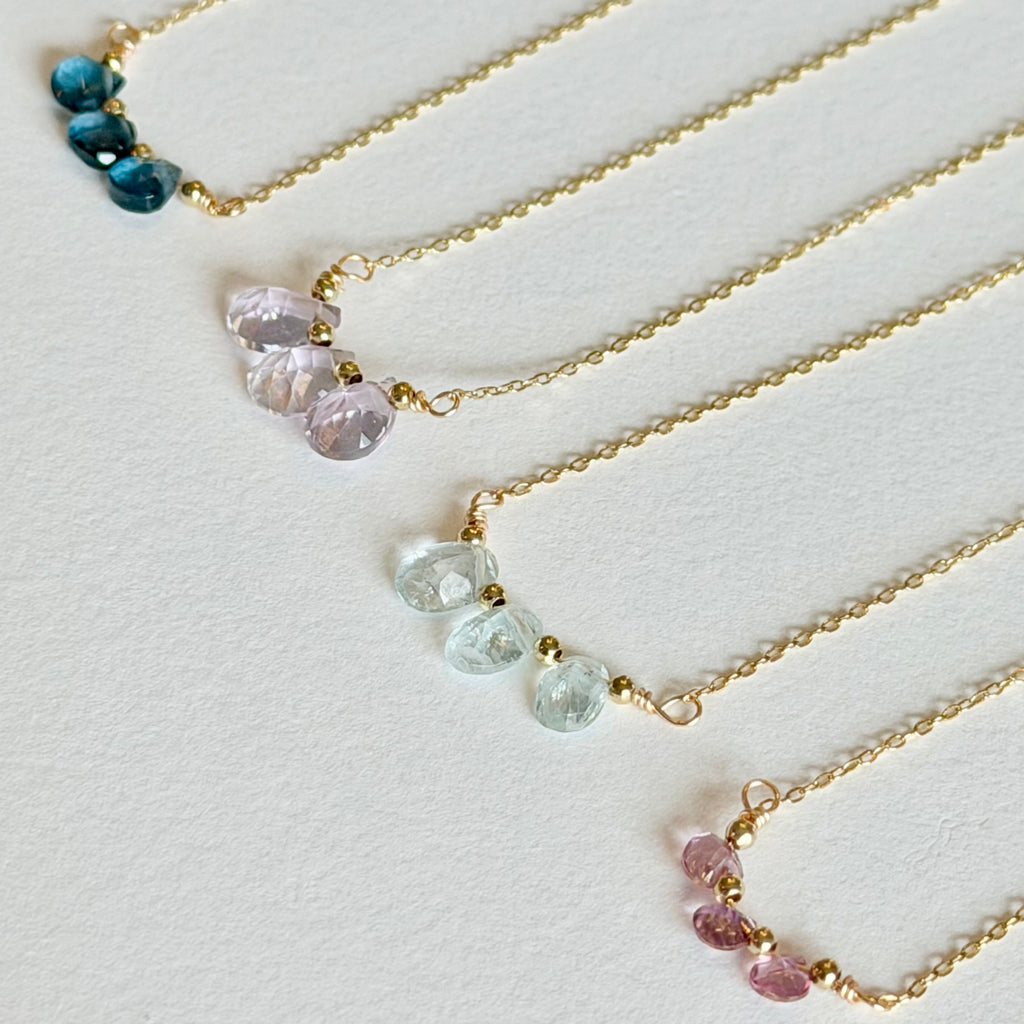 Set of four gold necklaces with beaded pendants on a light gray background
