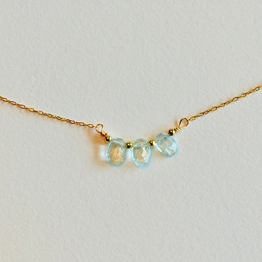 Gold necklace with three light blue gemstones on a light gray background