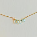 Gold necklace with three light blue gemstones on a light gray background