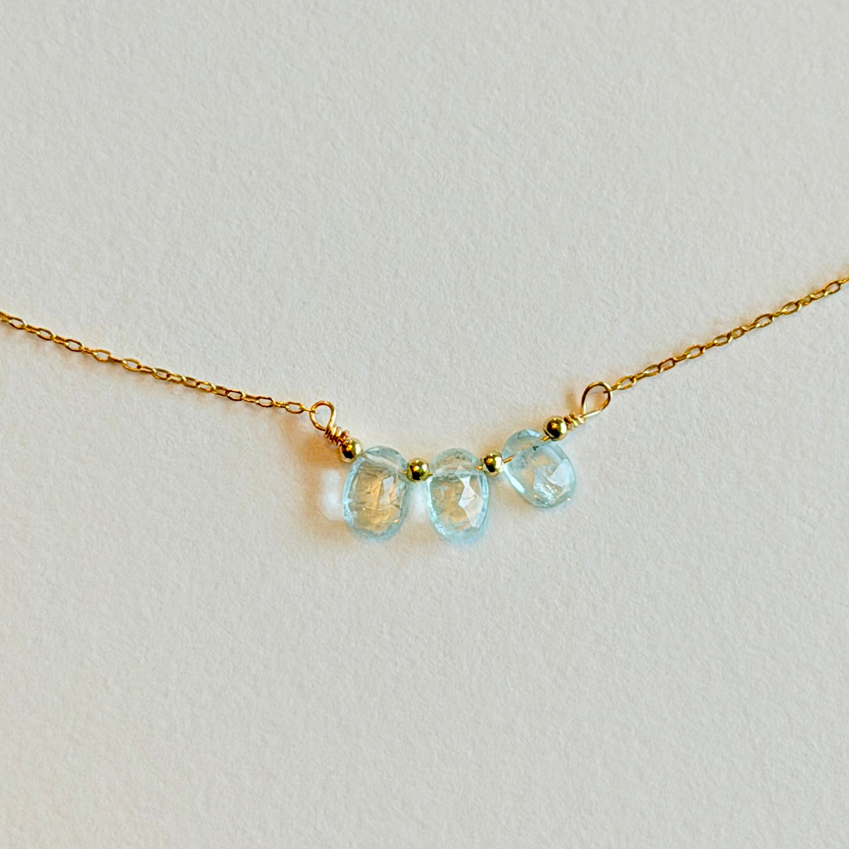 Gold necklace with three light blue gemstones on a light gray background