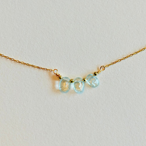 Gold necklace with three light blue gemstones on a light gray background