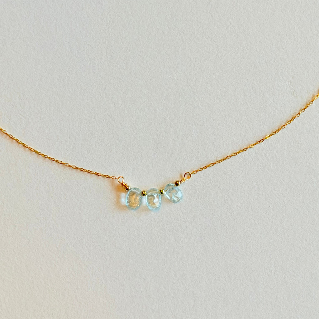 Delicate gold necklace with three light blue gemstones on a light gray background