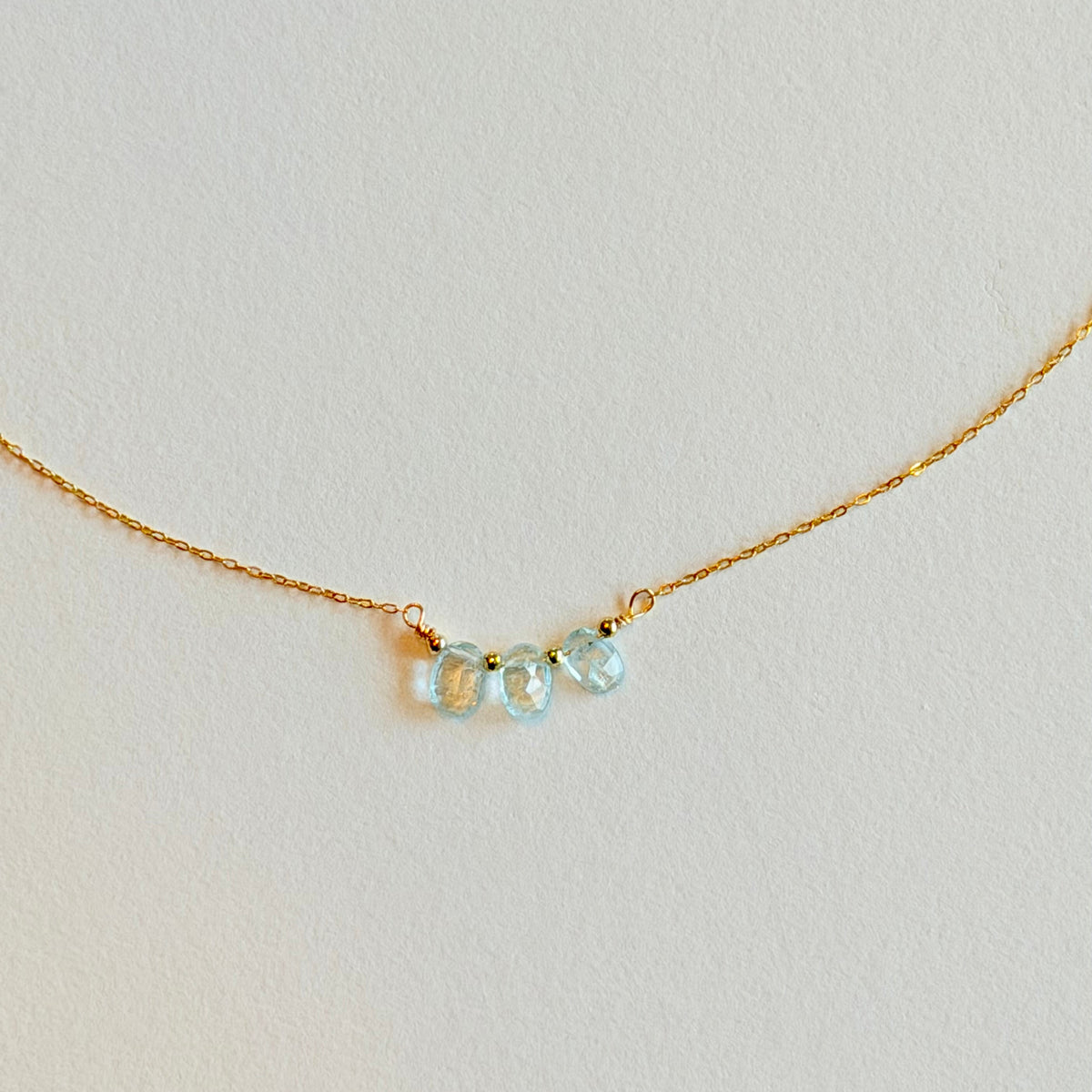 Delicate gold necklace with three light blue gemstones on a light gray background