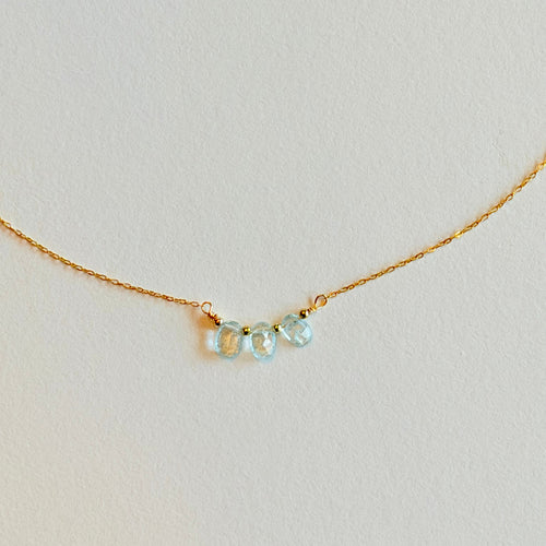 Delicate gold necklace with three light blue gemstones on a light gray background