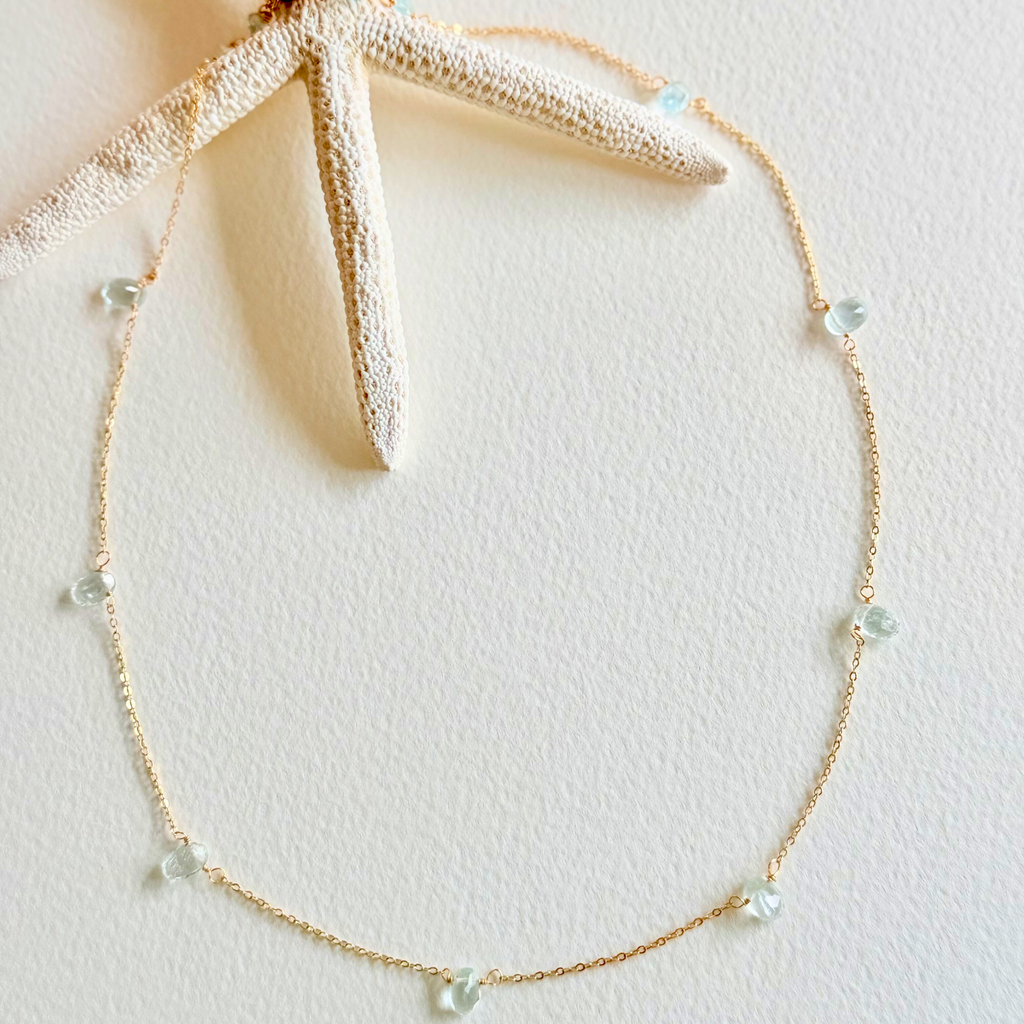 Gold necklace with small beads on a light pink background