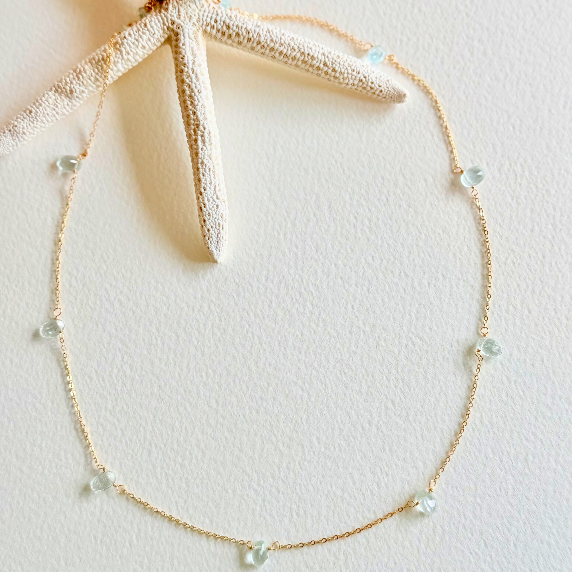 Gold necklace with small beads on a light pink background