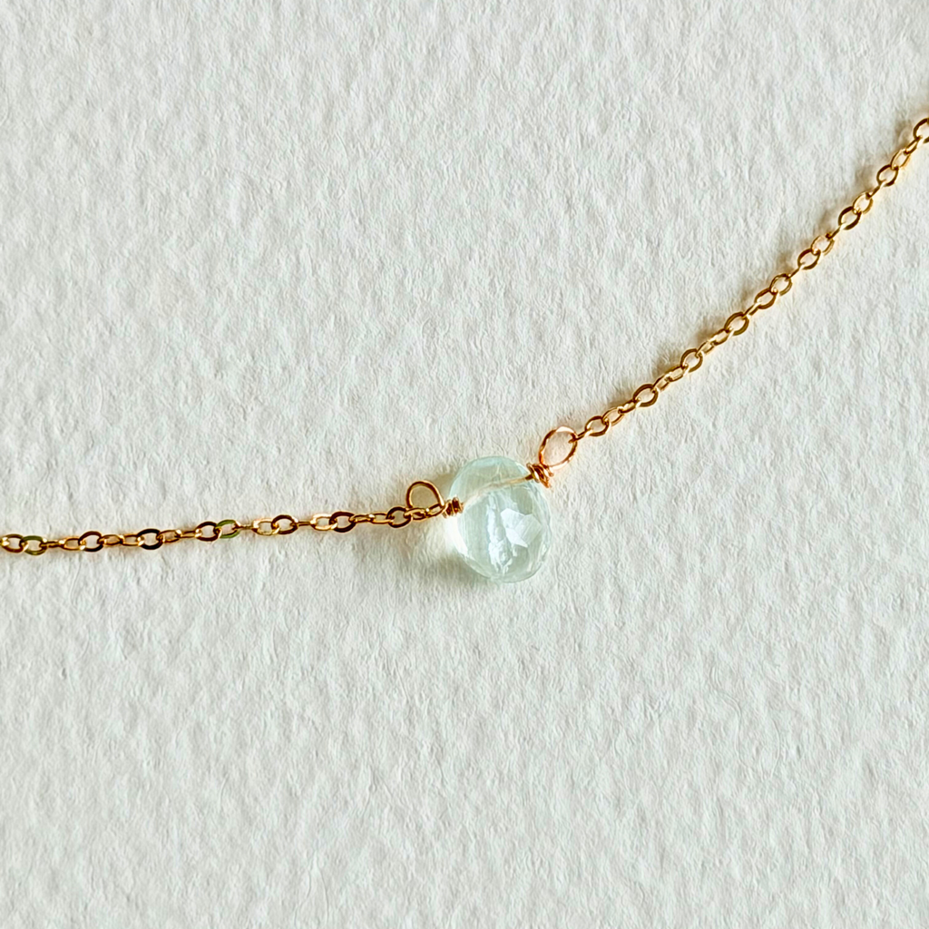 Gold necklace with a close up of single light blue gemstone on a white background