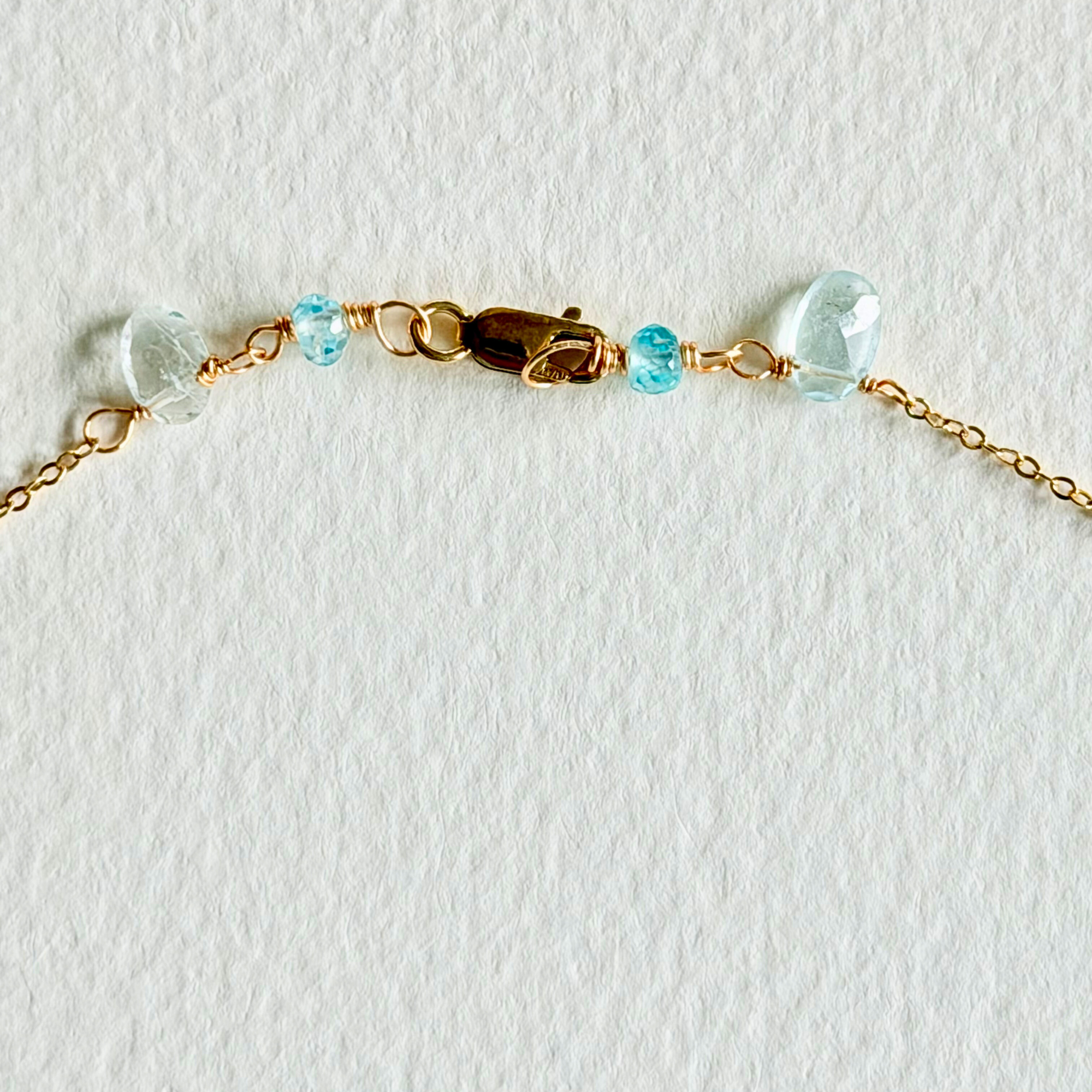 Gold bracelet with clear and blue beads on a white background