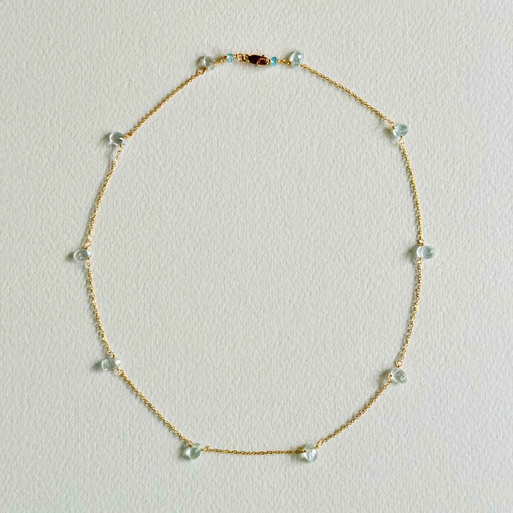 Delicate gold necklace with small beads on a light gray background