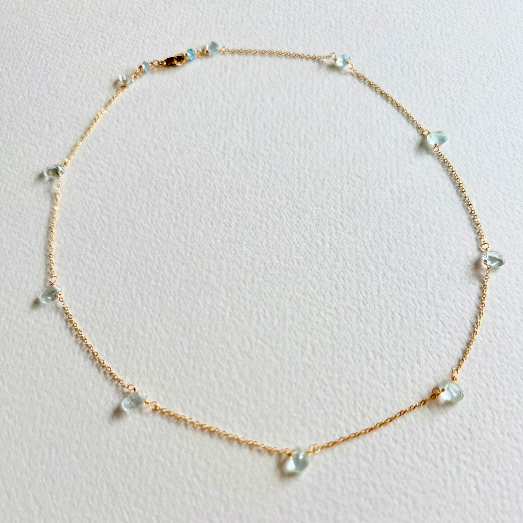 Delicate gold necklace with small beads on a light gray background