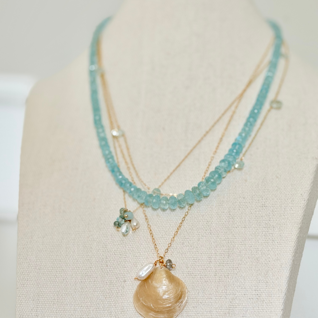 Necklace with turquoise beads and a shell pendant on a mannequin bust.
