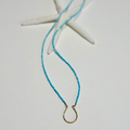 A delicate turquoise beaded necklace with a small gold horseshoe pendant, styled on a white surface with a white starfish prop.