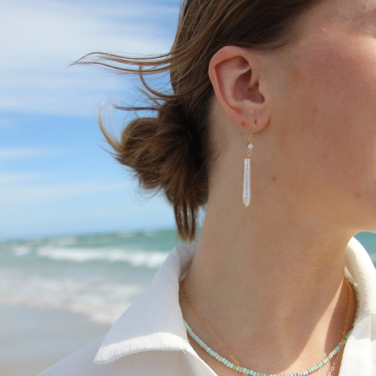 Person wearing earrings with a beach in the background
