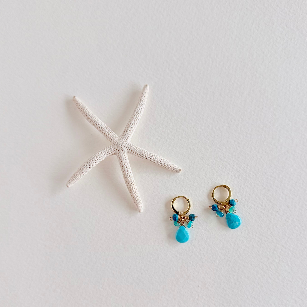 Pair of turquoise earrings with gold accents on a white surface with a starfish.