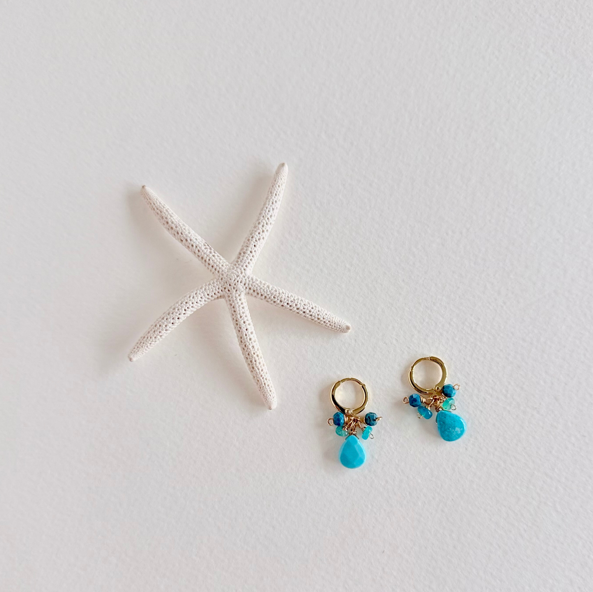 Pair of turquoise earrings with gold accents on a white surface with a starfish.