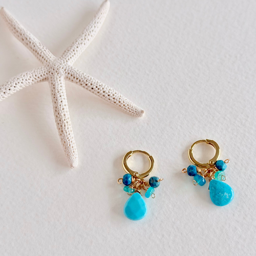 Gold hoop earrings with blue teardrop beads on a white background with a starfish.