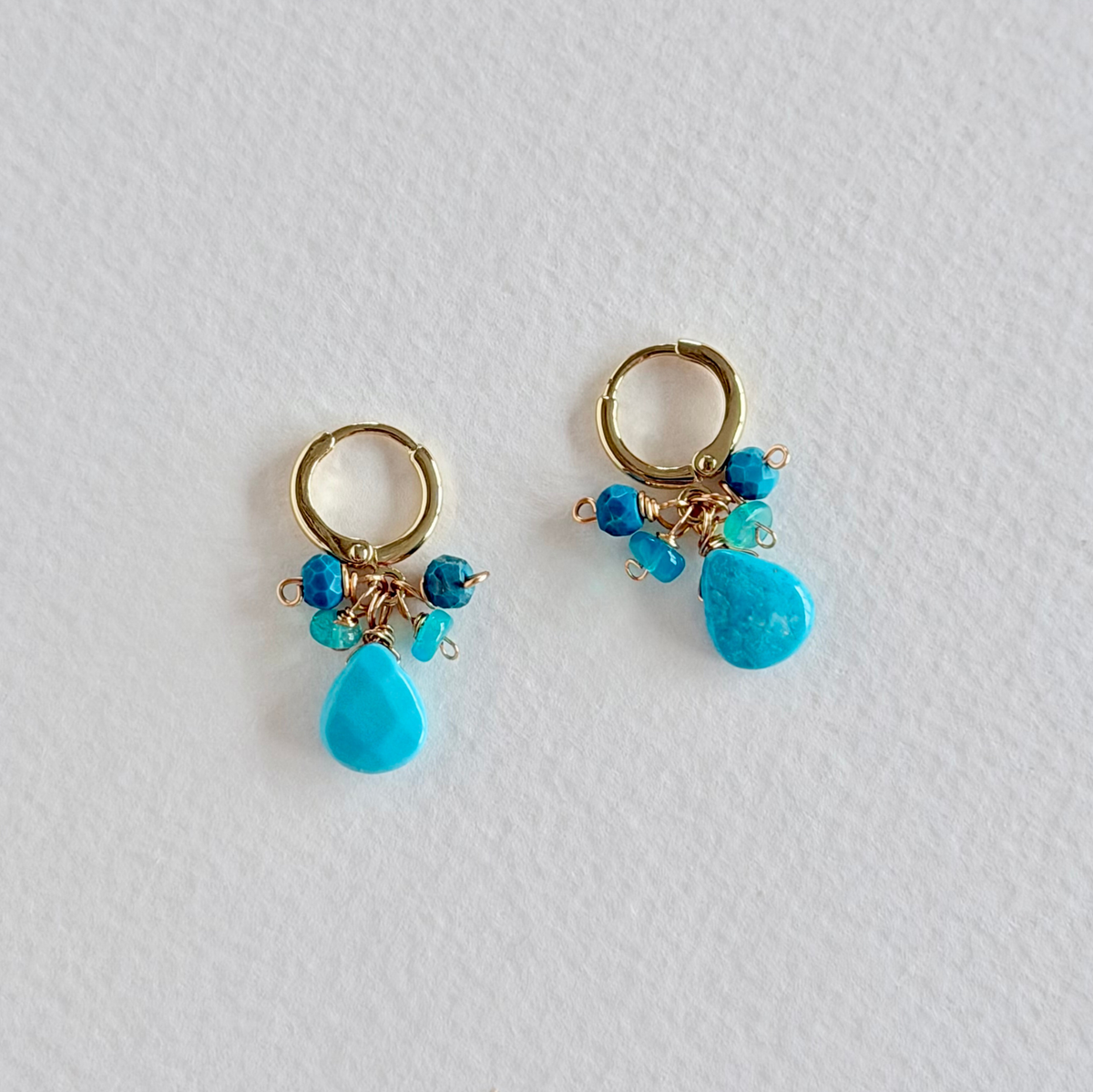 Pair of gold hoop earrings with turquoise beads on a light gray background
