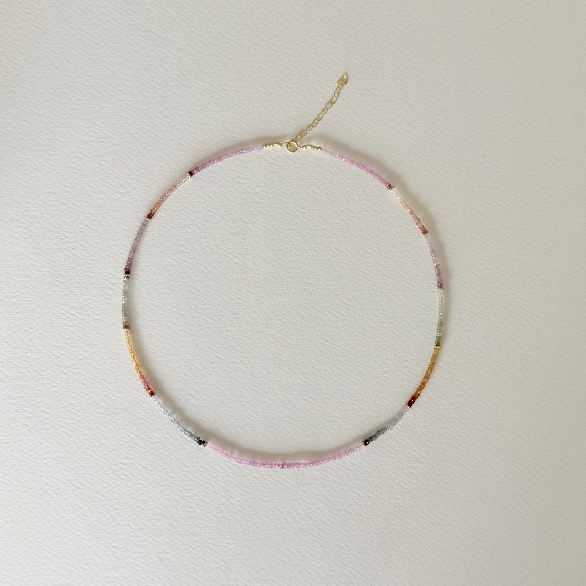 top down view of a multi colored sapphire necklace on a light background