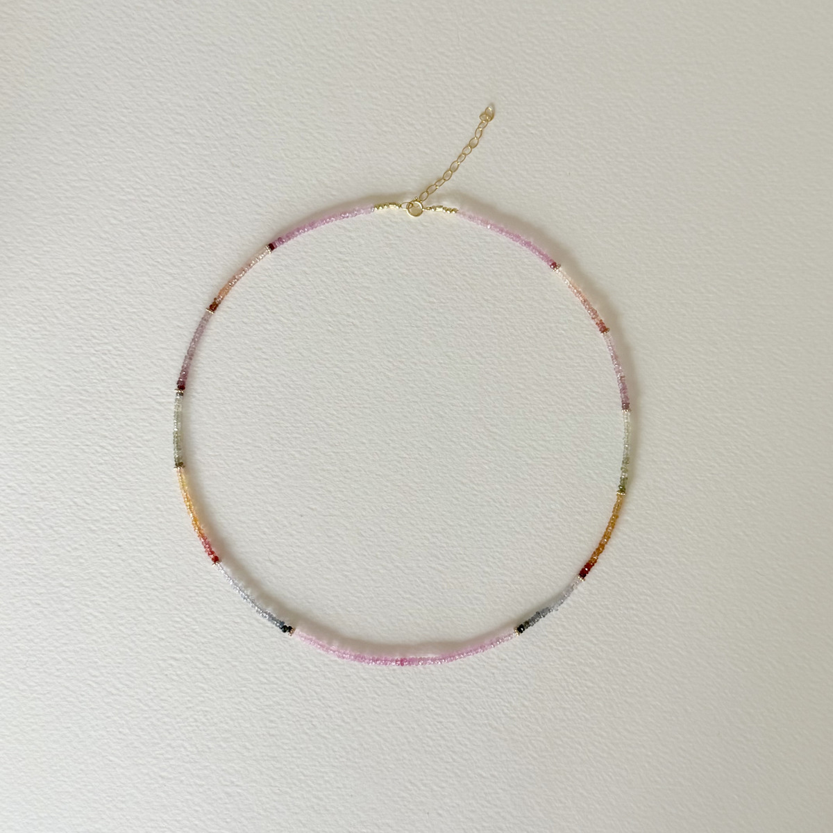 top down view of a multi colored sapphire necklace on a light background