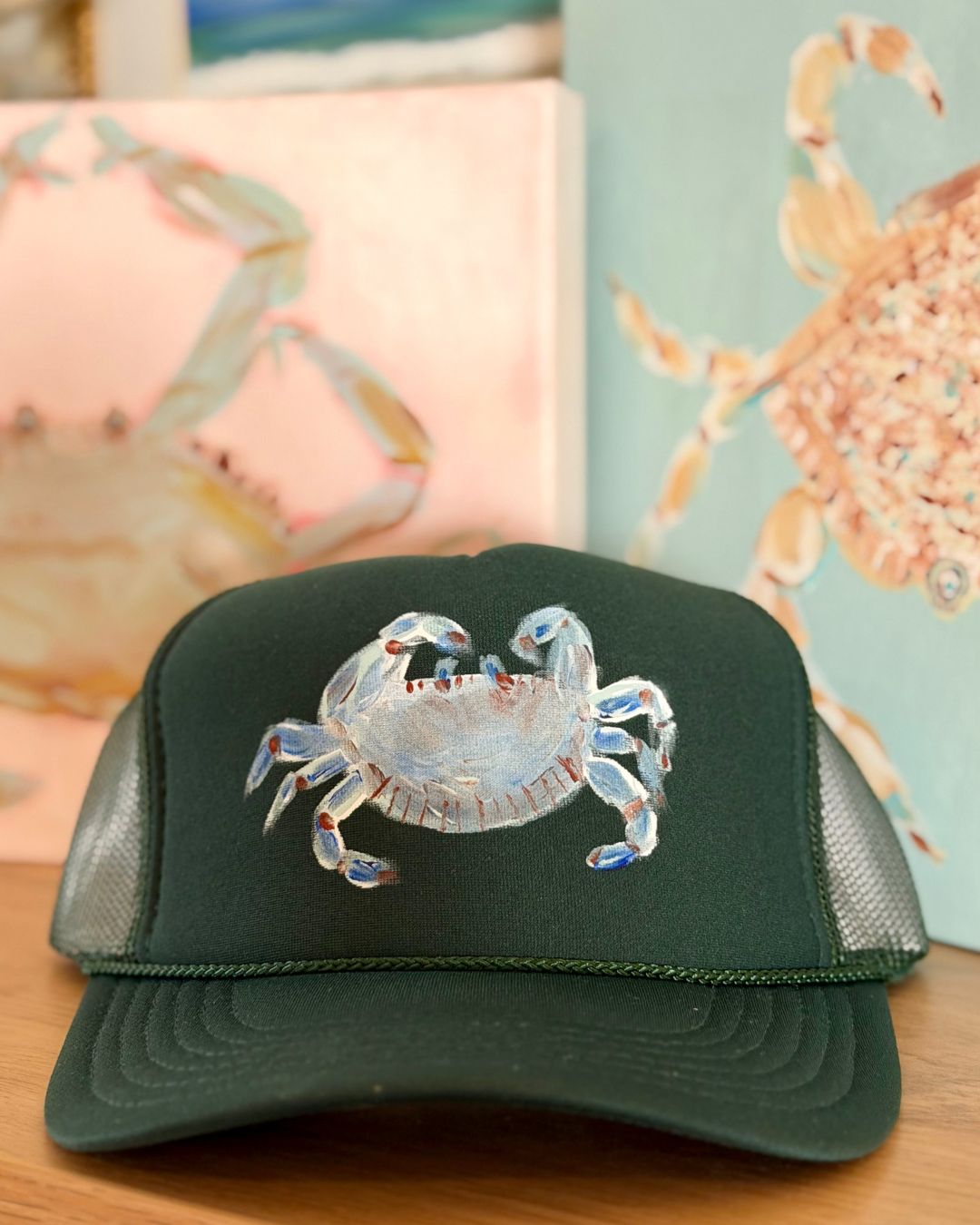 Dark green trucker hat featuring an original hand-painted blue crab in coastal blue and aqua tones by Marie & Oakley.