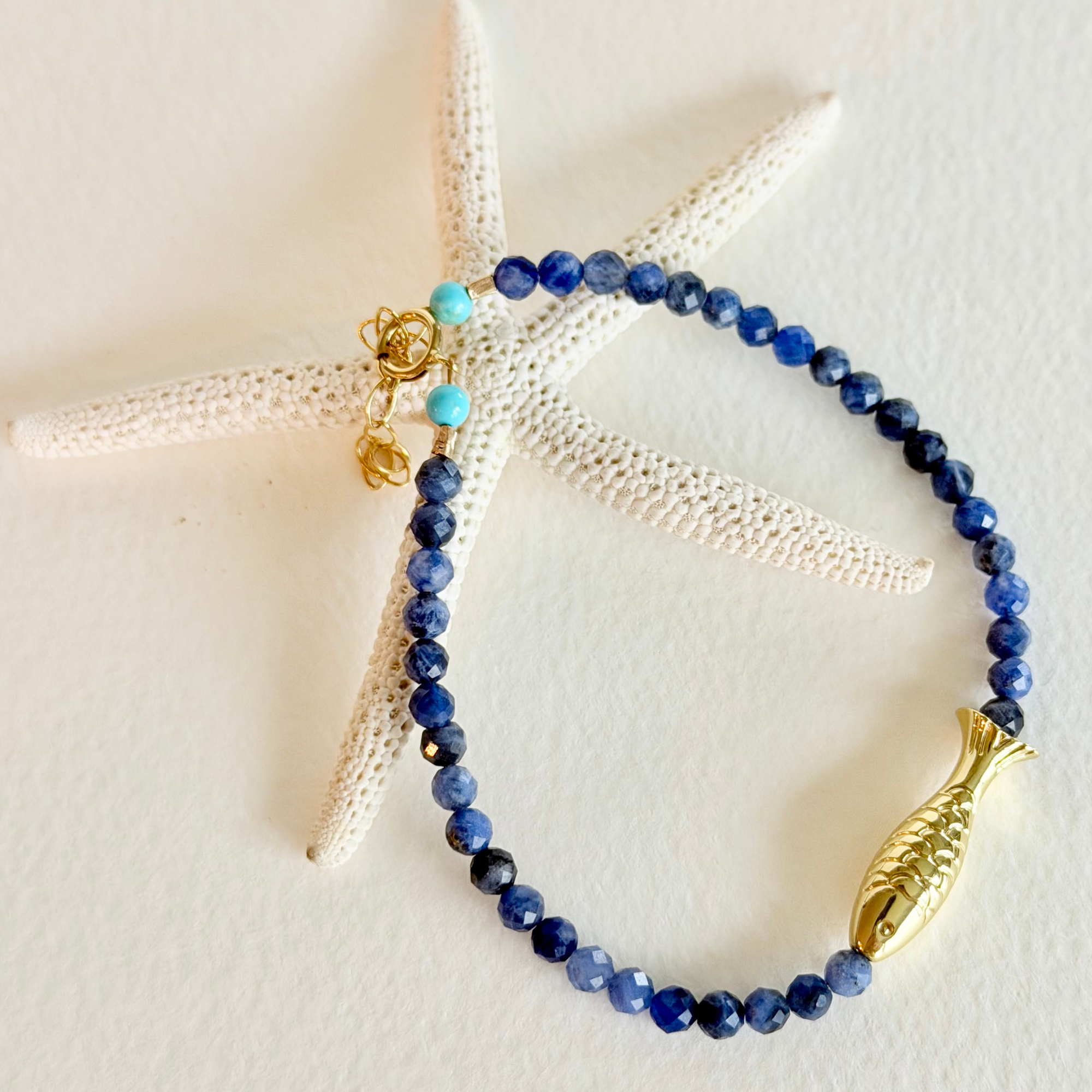 Blue beaded bracelet with gold fish charm on a starfish