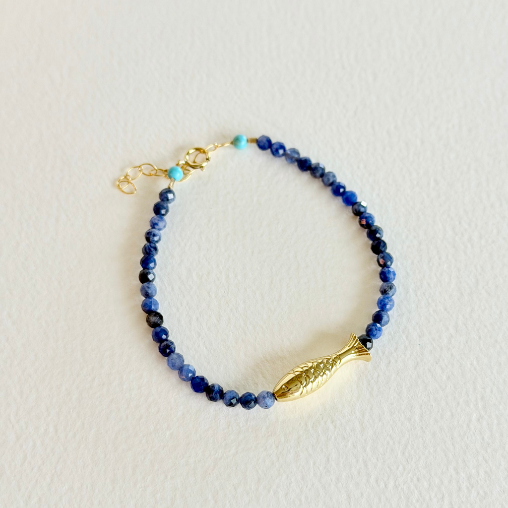 Beaded bracelet with a gold fish charm on a light background